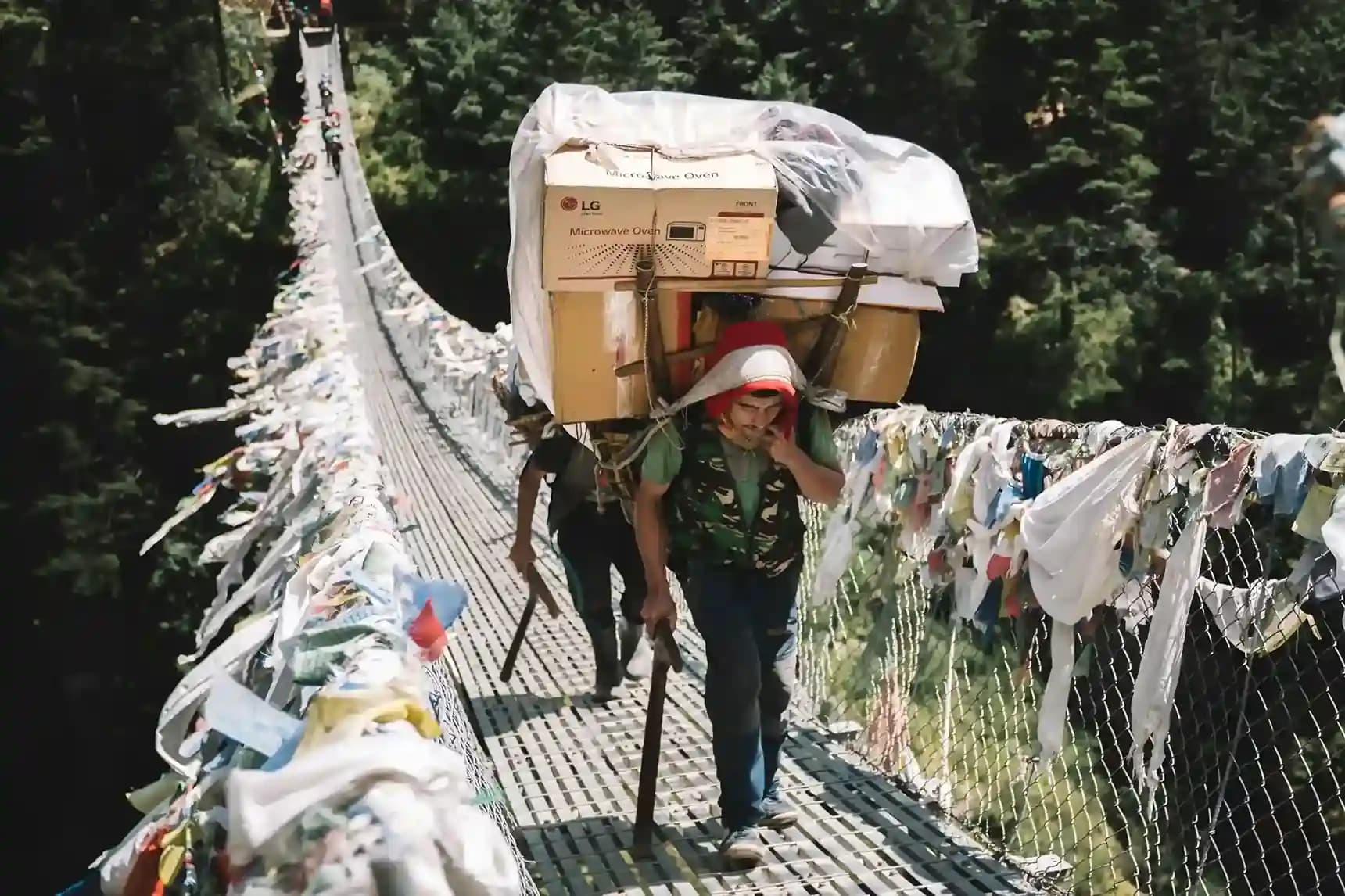 A caravan of porters crossing the high, prayer-flag-draped Hillary Suspension Bridge over the roaring Dudh Koshi River.